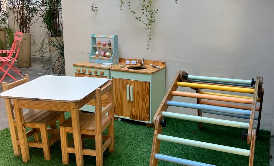 Espaço kids com mesa infantil, cozinha de brinquedo e estrutura de escalada no Que Doce.